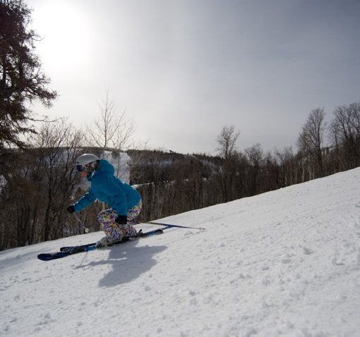 profile view of a skier carving down a groomed run