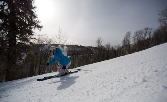 profile view of a skier carving down a groomed run