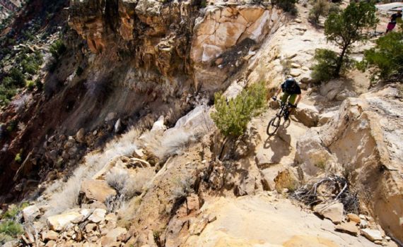 rider mountian bikes along the edge of a rocky cliff on a sunny day