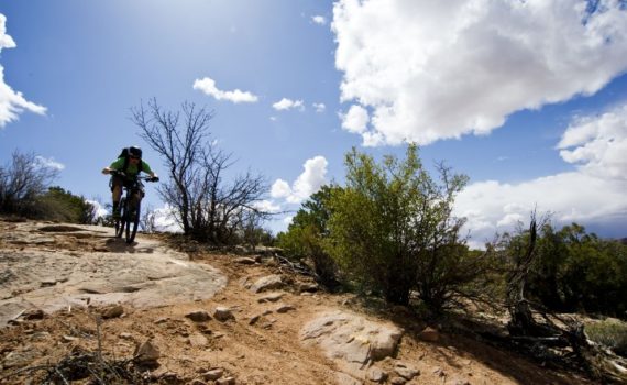 blue sky and puffy white clouds above a mountain biker riding down some slickrock