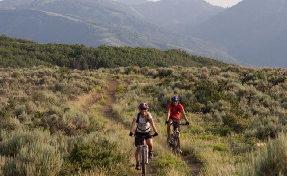 two mountain bikers smile as they ride along a mellow double track trail