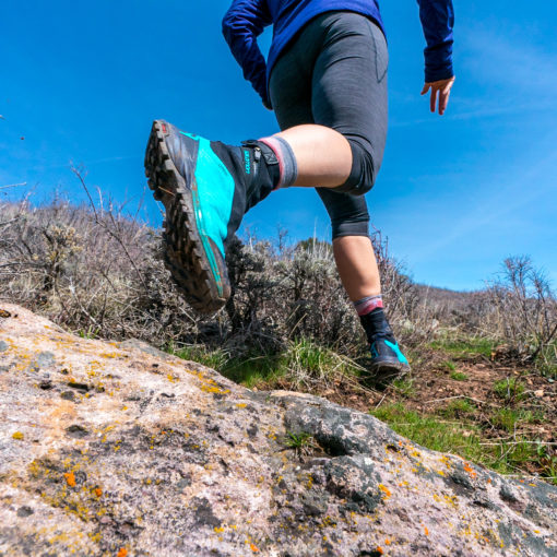 low-to-ground perspective looking up at traill running shoes in action over a rocky landscape