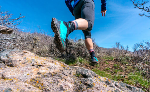 low-to-ground perspective looking up at traill running shoes in action over a rocky landscape