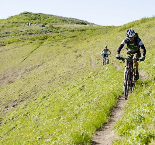 two mountain bikers ride along a cross-mountain trail, coming toward the photographer