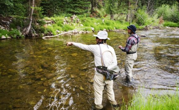 fly fishing guide points out where to cast while wading with an angler client in a small river
