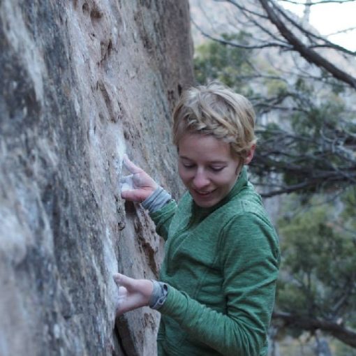 rock climber smiling about an undercling jug, wearing layers of technical clothing