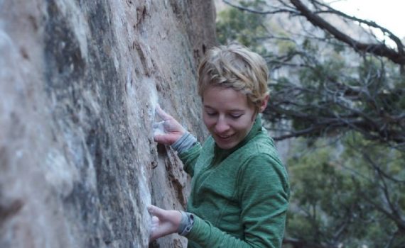 rock climber smiling about an undercling jug, wearing layers of technical clothing
