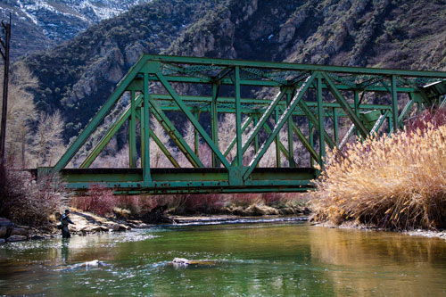 A fisherman fishes in front of a green bridge