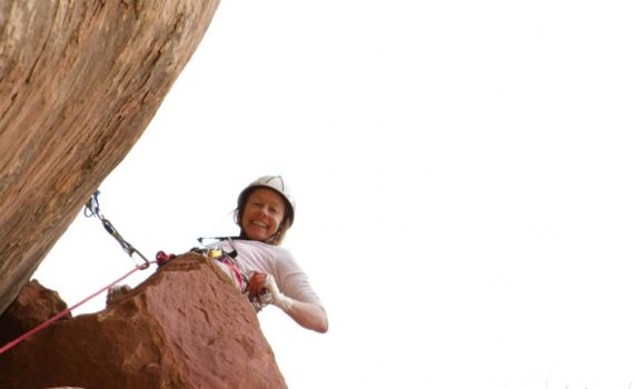 rock climber leading a climb pauses to smile down at the camera