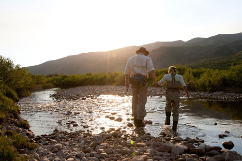 a older fisherman stands with a young fisherman in a river