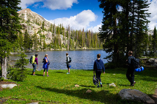 Climbers stand in green clearing at base of rock face
