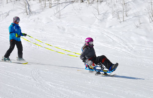 a sit skiers learns how to ski with a guide behind