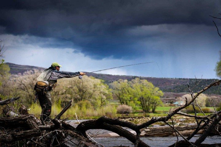Fisherman casts into river with dark clouds in background