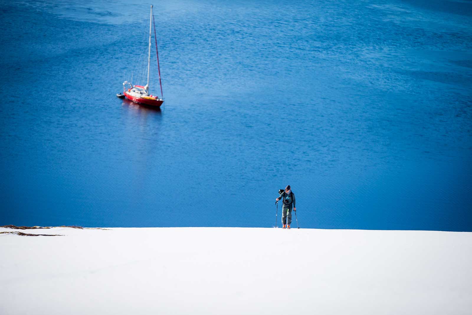 Skier climbs hill with boat in the background
