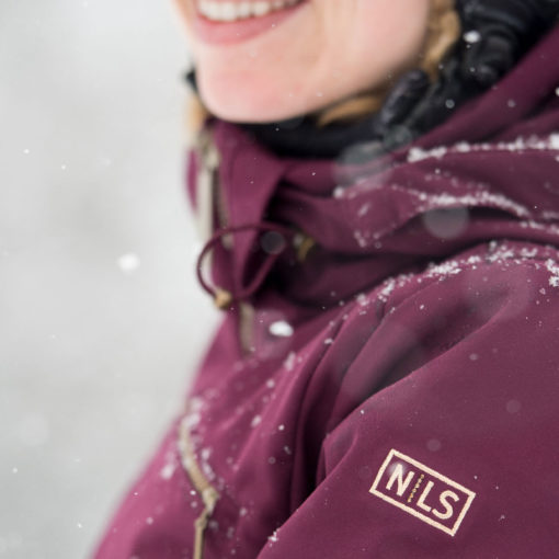 close -cropped image of a skier's smiling above a snow-dusted burgundy color jacket