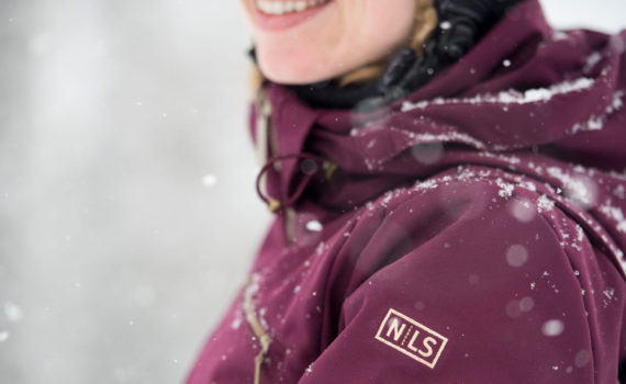 close -cropped image of a skier's smiling above a snow-dusted burgundy color jacket