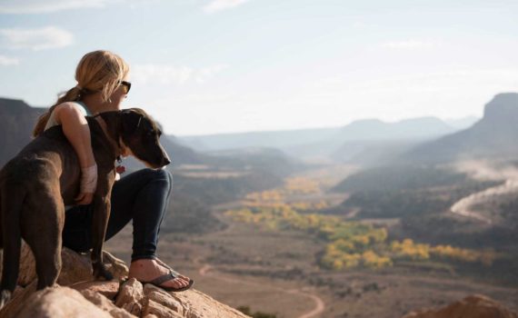 A woman looks out over a desert landscape witha dog