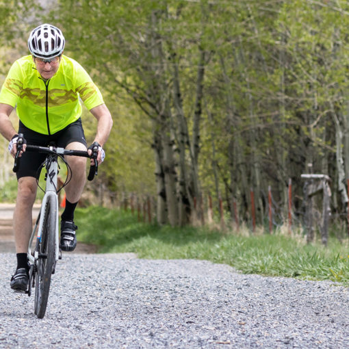 cyclist in a yellow jersey riding on a gravel trail surrounded by aspen trees