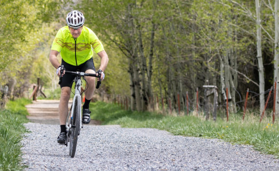 cyclist in a yellow jersey riding on a gravel trail surrounded by aspen trees