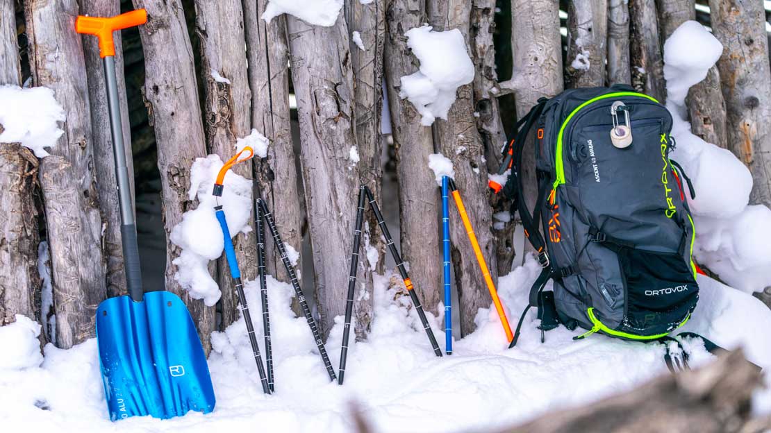 Shovel, probe, and avalanche airbag rest against ski hut
