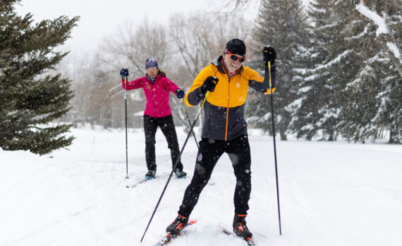 Two Nordic skiers skiing through snowfall near the White Pine Touring Center in Park City, UT