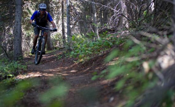 Charlie Sturgis mountain biking on a trail through a forest in Park City, UT