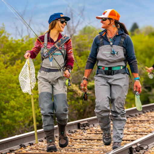 Four women with fly fishing gear walk down a rail road track near a river in Northern Utah