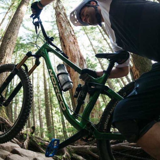 A mountain biker pushes a norco bike up a trail in a heavily wooded area