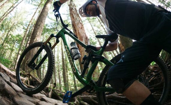 A mountain biker pushes a norco bike up a trail in a heavily wooded area