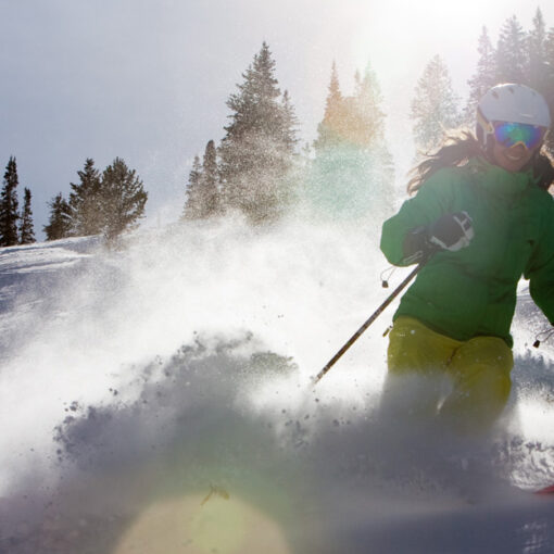 A woman skiing through deep powder with snow-covered trees in the background, her face beaming with joy as the sun shines brightly behind her. The golden light casts a hopeful glow, symbolizing a bright future for the outdoor industry.