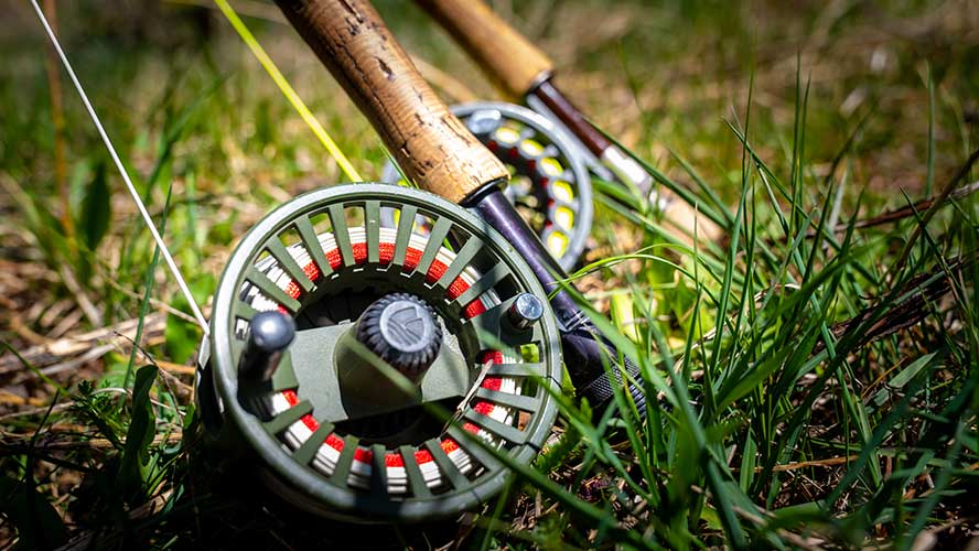 An upclose look at a fishing reel next to another fly rod.