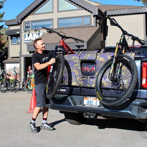 Jans Expert loads a specialized bike into the back of a truck on a sunny day in front of the Jans Bike shop entrance.