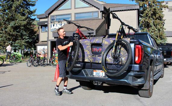 Jans Expert loads a specialized bike into the back of a truck on a sunny day in front of the Jans Bike shop entrance.