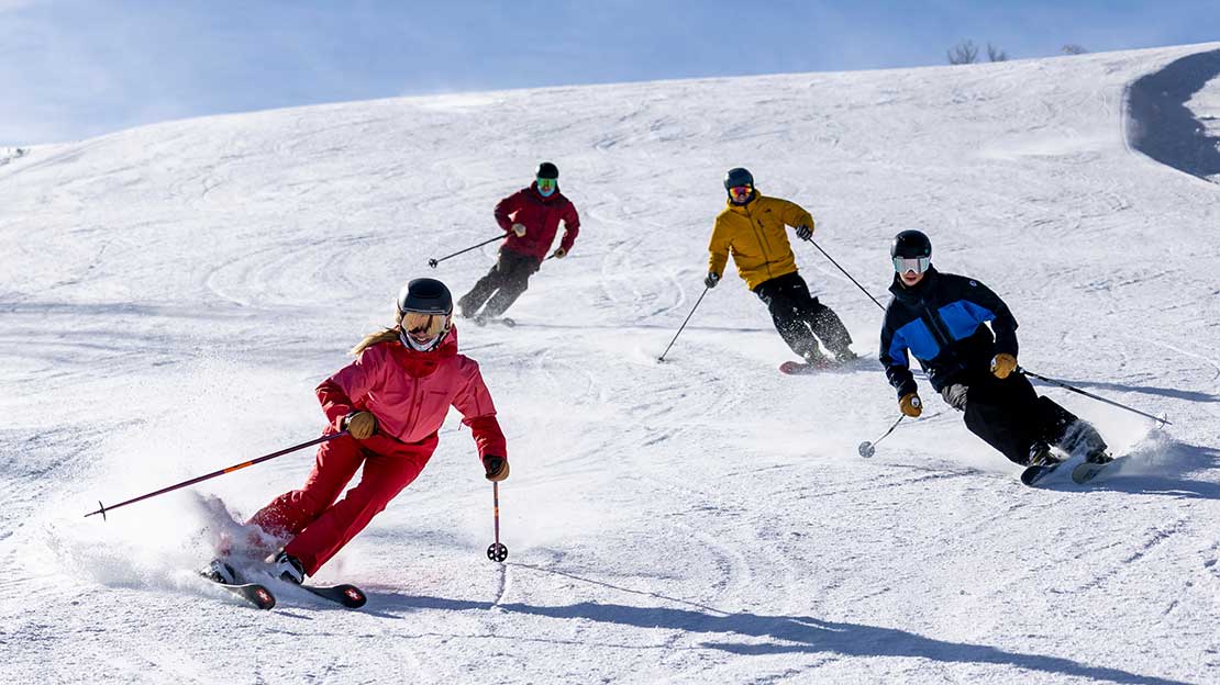 Four expert skiers from the Jans team skiing on a groomed run during a blue-sky day at Deer Valley Resort, Park City, UT