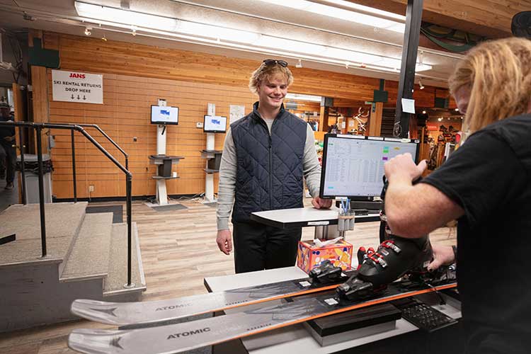 Jans rental shop shows a tech fitting a boot to a rental ski for a happy customer