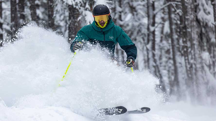 Jans Expert skiing through trees in deep powder snow that is flying up over his waist as he turns at Deer Valley Resort, Park City, Utah.